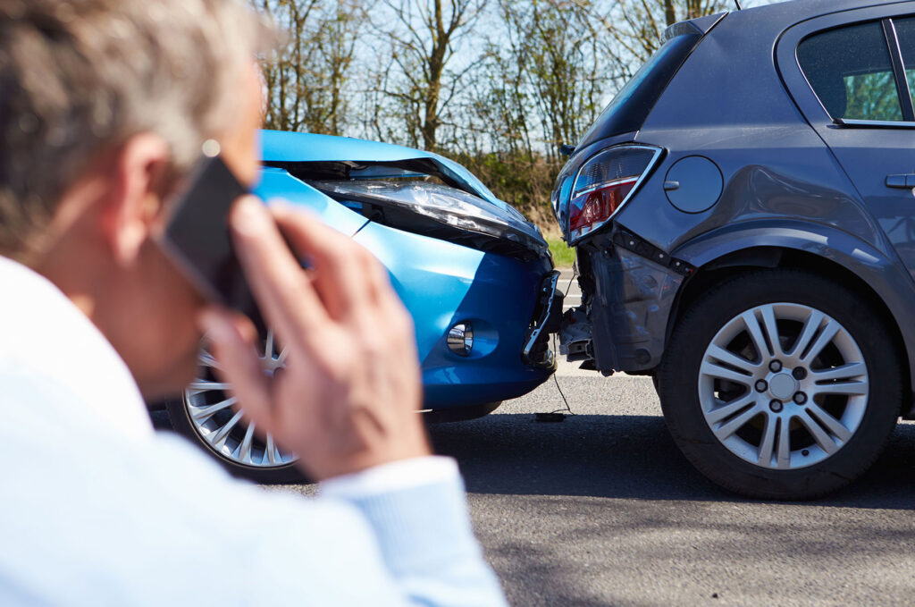Man calling on a mobile phone after a rear-end car accident, with two damaged vehicles stopped on the road. Man calling on a mobile phone after a rear-end car accident, with two damaged vehicles stopped on the road.