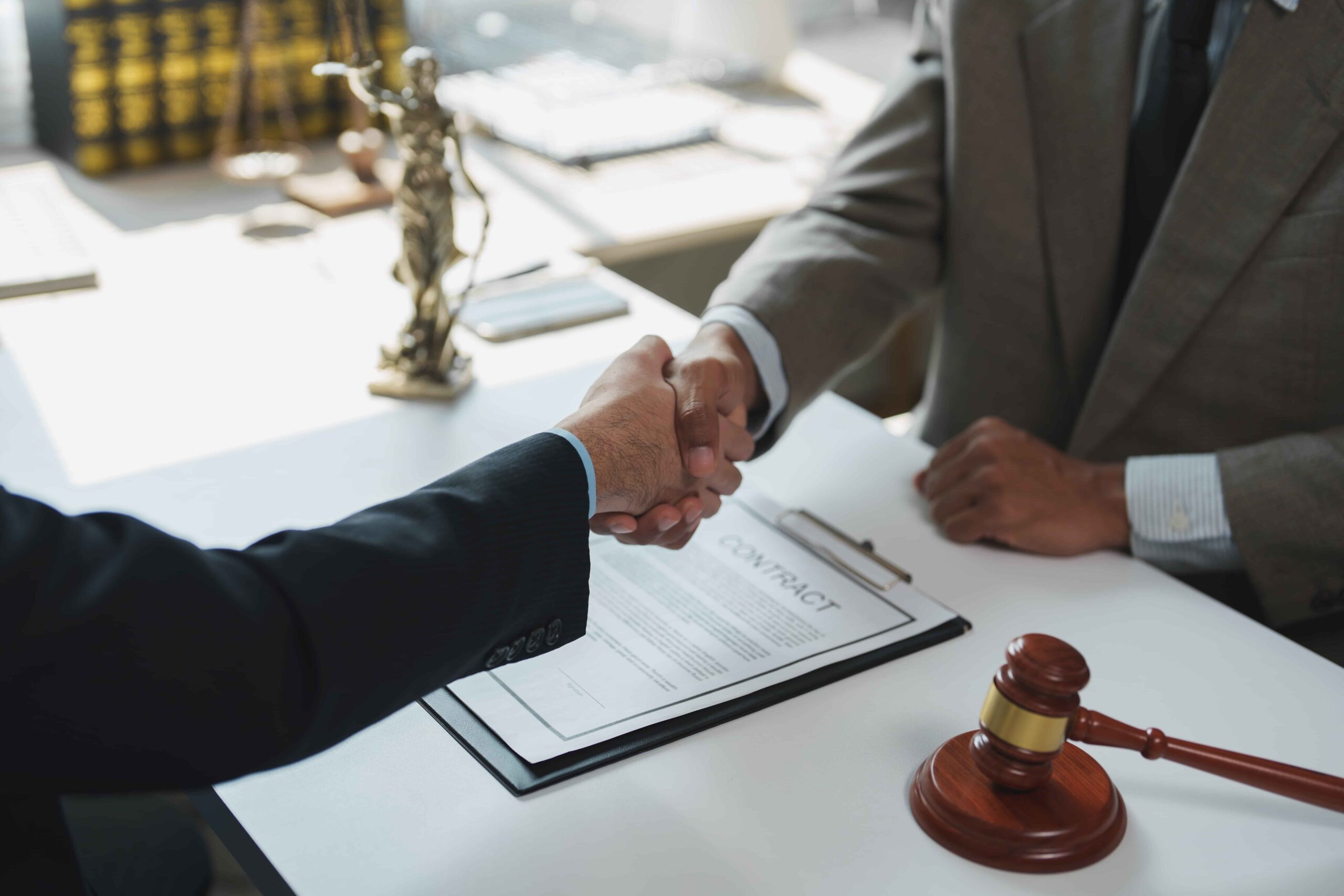 Attorneys shaking hands over a signed contract with a judge’s gavel on the desk, symbolizing a legal agreement or settlement.