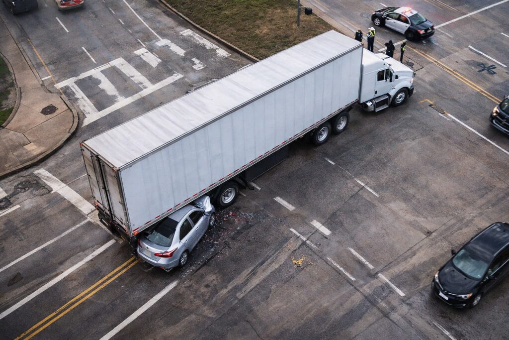 Aerial view of a wide turn truck accident at a Houston intersection showing an 18-wheeler trapping a passenger car during a turn. Aerial view of a wide turn truck accident at a Houston intersection showing an 18-wheeler trapping a passenger car during a turn.