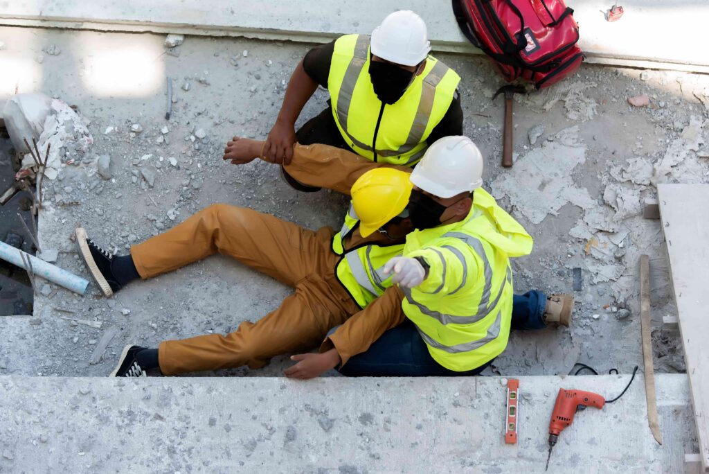 Construction workers assisting injured colleague at job site after workplace accident, highlighting construction site safety and workers’ compensation concept Construction workers assisting injured colleague at job site after workplace accident, highlighting construction site safety and workers’ compensation concept