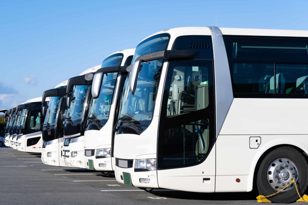 Row of white coach buses parked in a lot, representing commercial transportation services and fleet management operations Row of white coach buses parked in a lot, representing commercial transportation services and fleet management operations