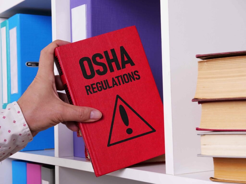 Hand holding OSHA regulations book on shelf, representing workplace safety standards, compliance, and occupational health laws Hand holding OSHA regulations book on shelf, representing workplace safety standards, compliance, and occupational health laws