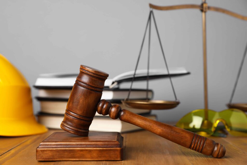 Judge’s gavel with scales of justice, books, and safety helmet on desk, representing construction law, workplace injury claims, and legal litigation Judge’s gavel with scales of justice, books, and safety helmet on desk, representing construction law, workplace injury claims, and legal litigation