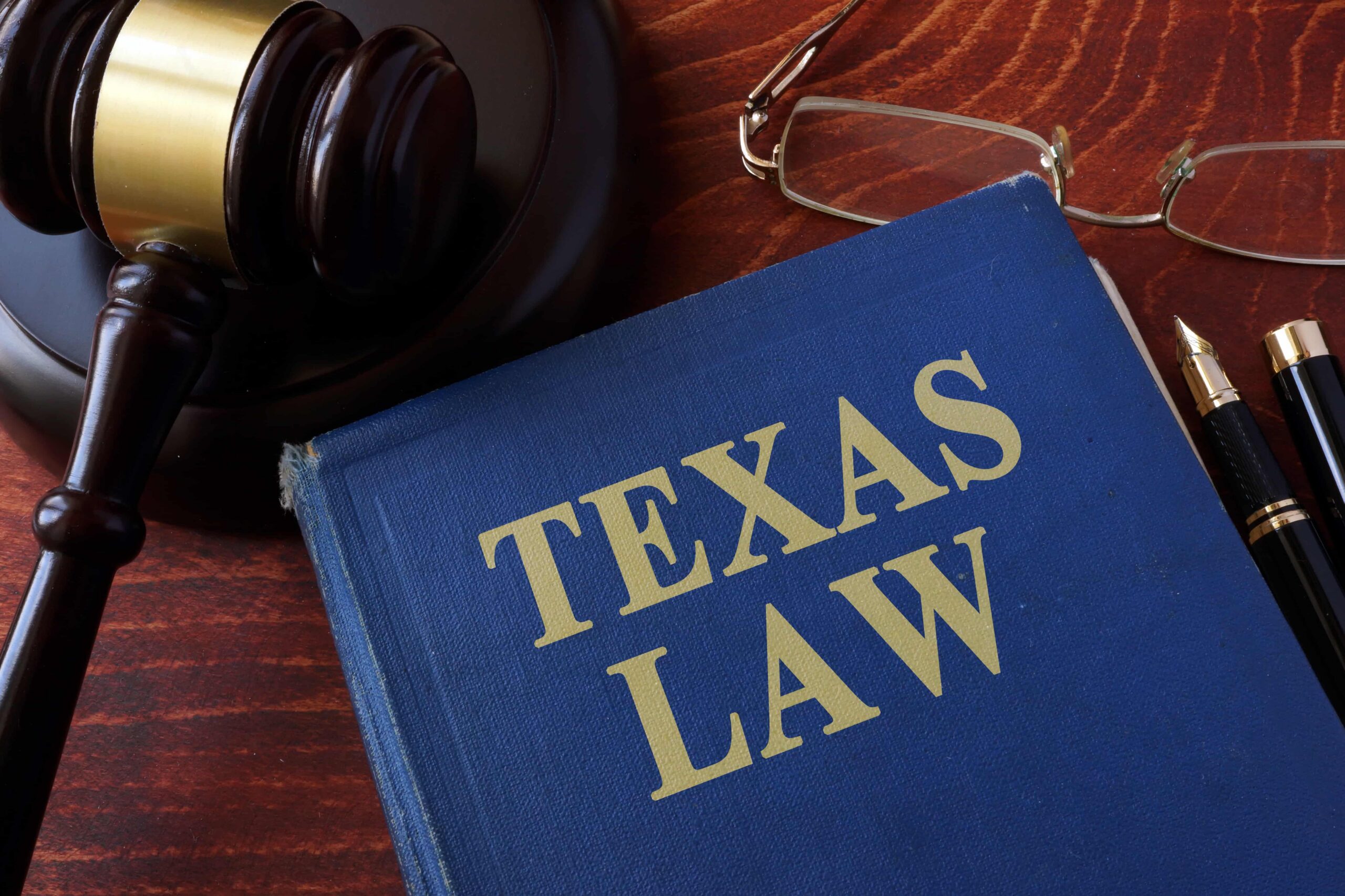 Texas law book with judge’s gavel, eyeglasses, and pen on wooden desk representing legal services and litigation in Texas