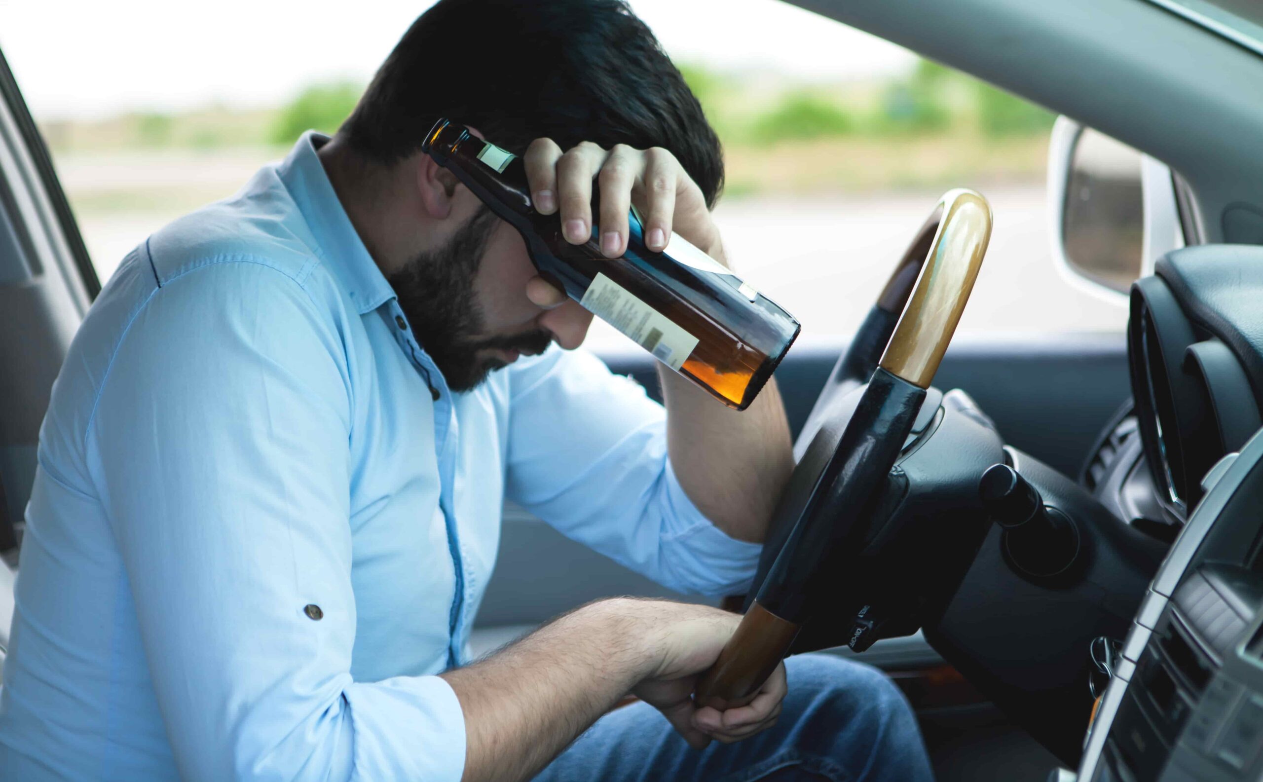 Man sitting in the driver’s seat holding a beer bottle with his head down on the steering wheel, representing drunk driving and DUI risk.