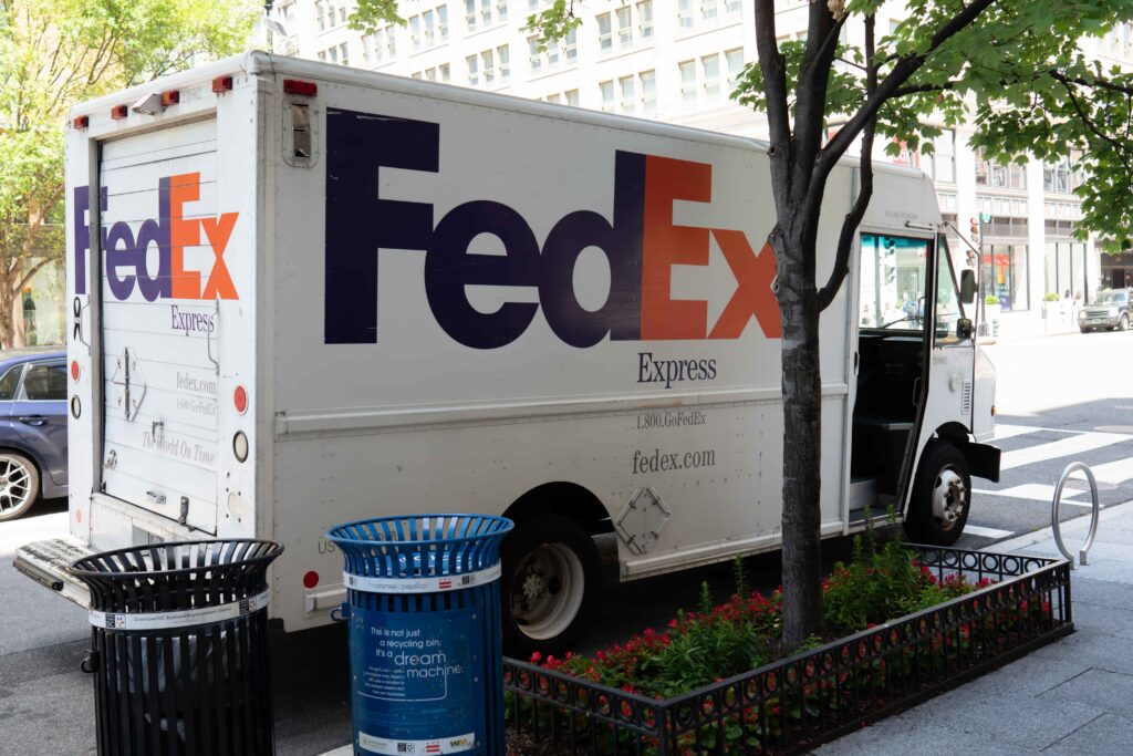 FedEx Express delivery truck parked on a city street near a sidewalk and buildings, representing package shipping and courier delivery services. FedEx Express delivery truck parked on a city street near a sidewalk and buildings, representing package shipping and courier delivery services.
