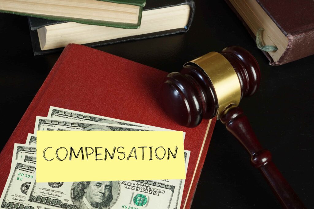 Judge&rsquo;s gavel, law books, and US dollar bills with a &ldquo;Compensation&rdquo; note, symbolizing financial compensation or legal settlement in a lawsuit.