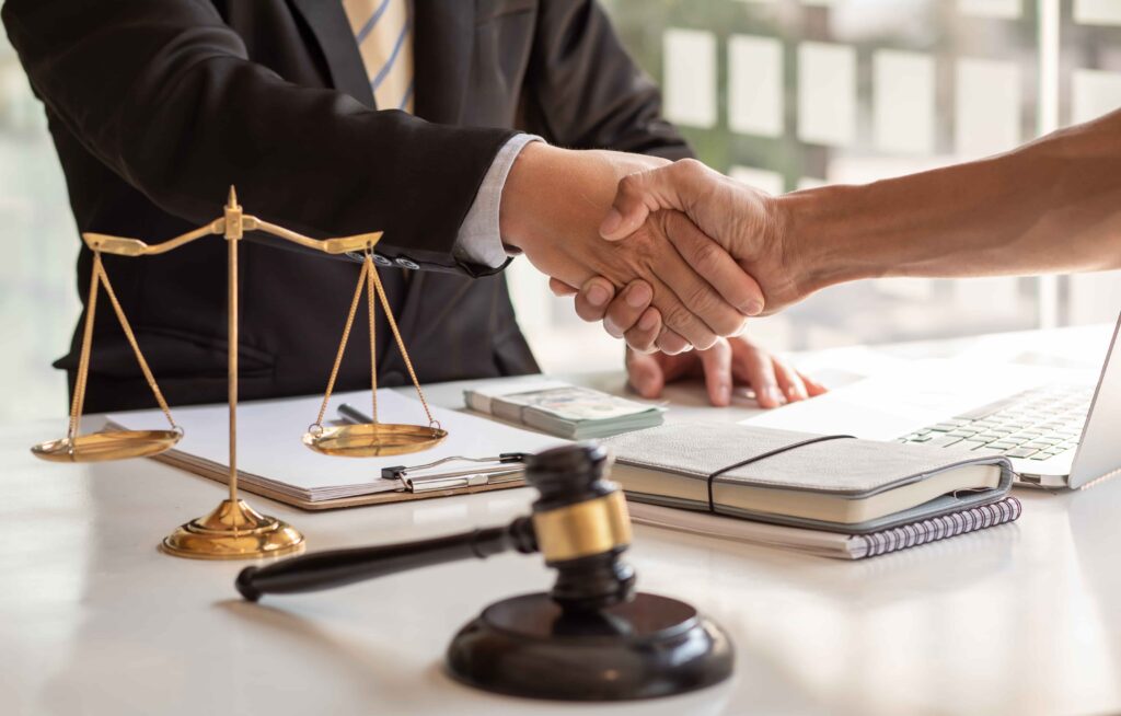 Lawyer shaking hands with client at desk with scales of justice and gavel, representing legal agreement, settlement, or personal injury case resolution