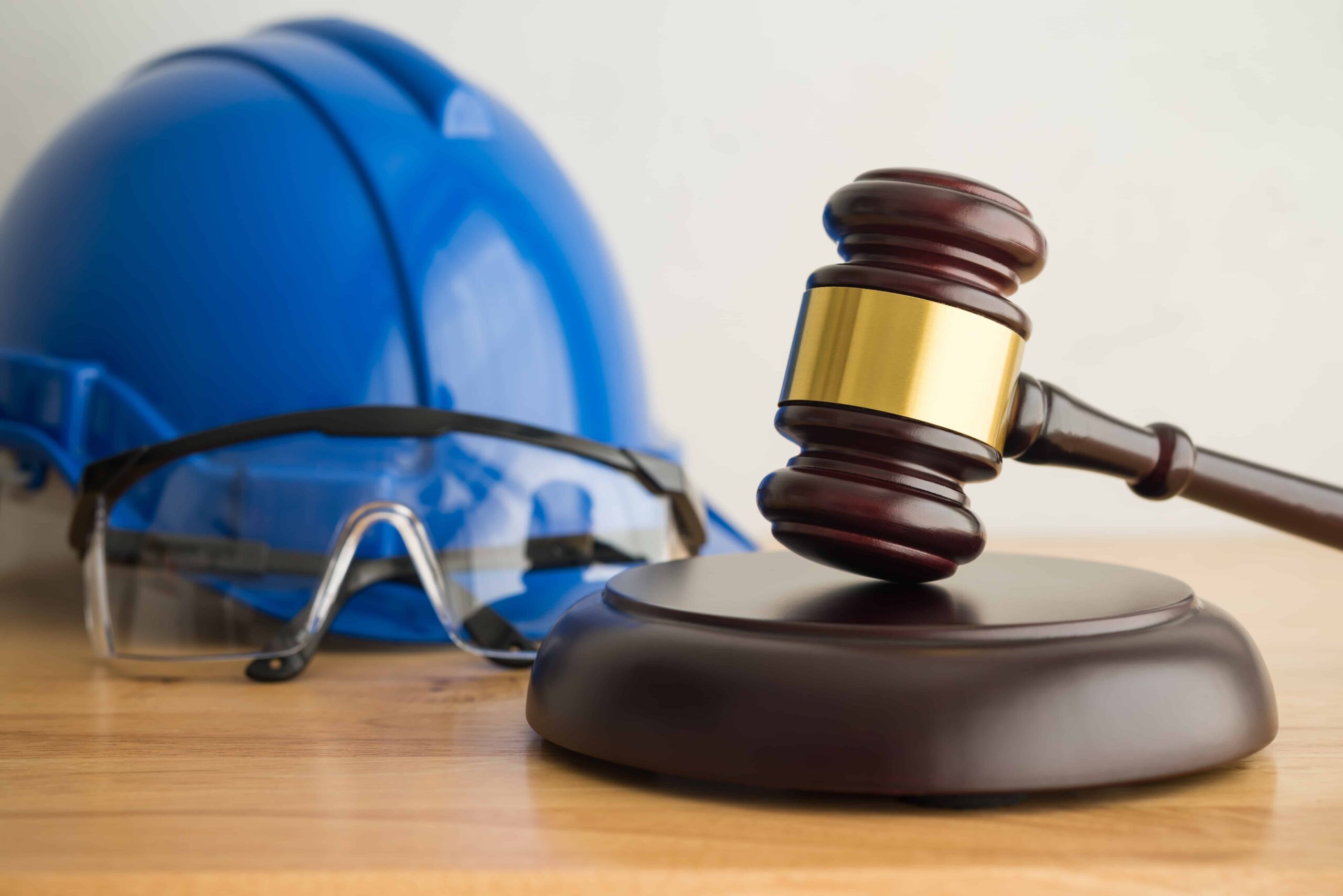 Judge’s gavel with safety helmet and protective glasses, representing workplace injury law, construction accidents, and legal safety compliance