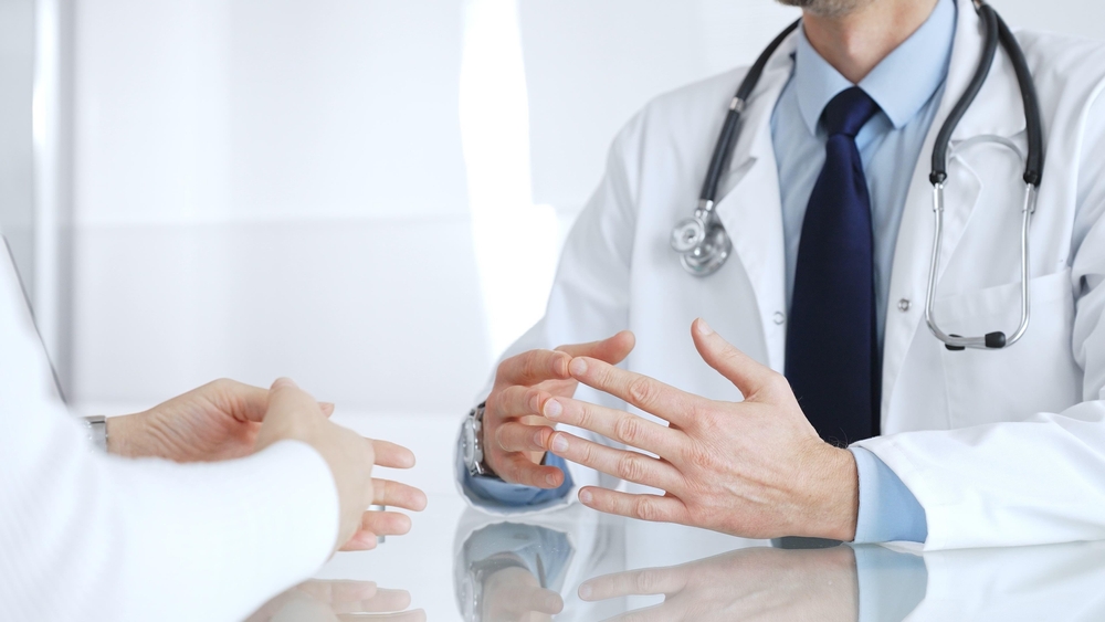 A doctor consults with a patient across a desk, sharing medical news